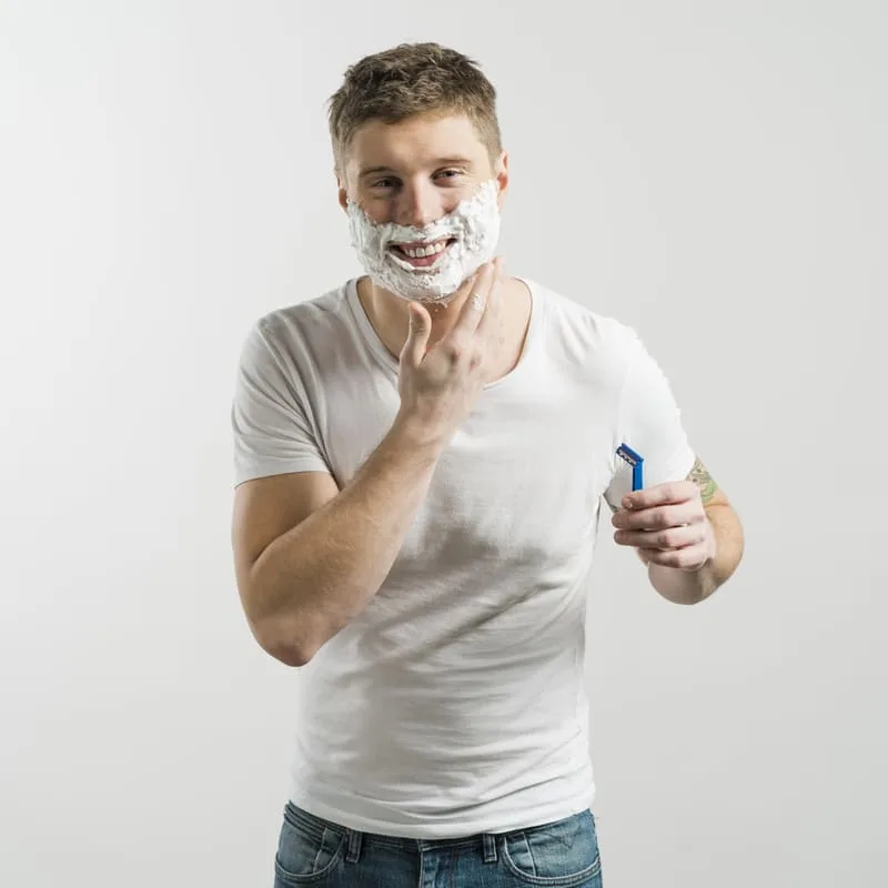 close-up-smiling-young-man-with-shaving-foam-his-face-holding-razor-hand-looking-camera